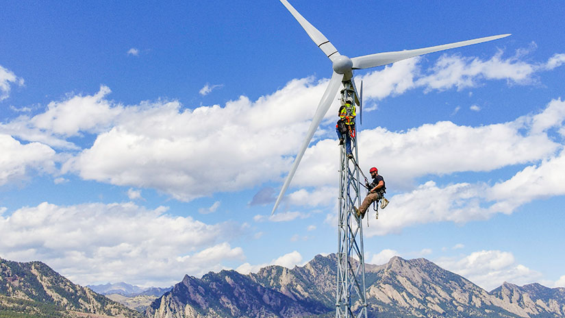 20240228-newsletter-bergey-installation Two people climb a wind turbine with mountains in the background.