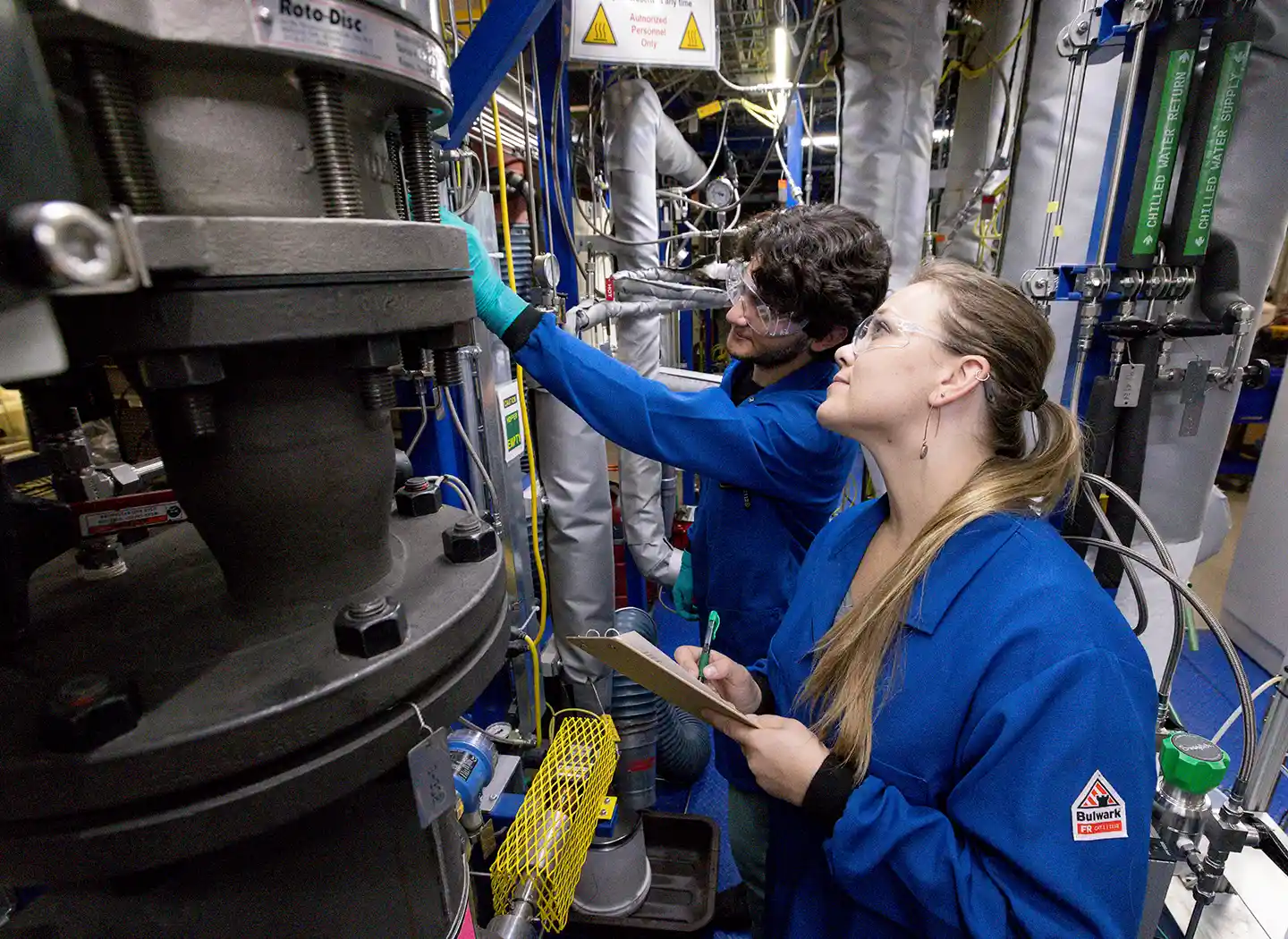 Two researchers visually inspect the Pyrolyzer biomass feeder in the Davison Circulating Riser laboratory at NLR.