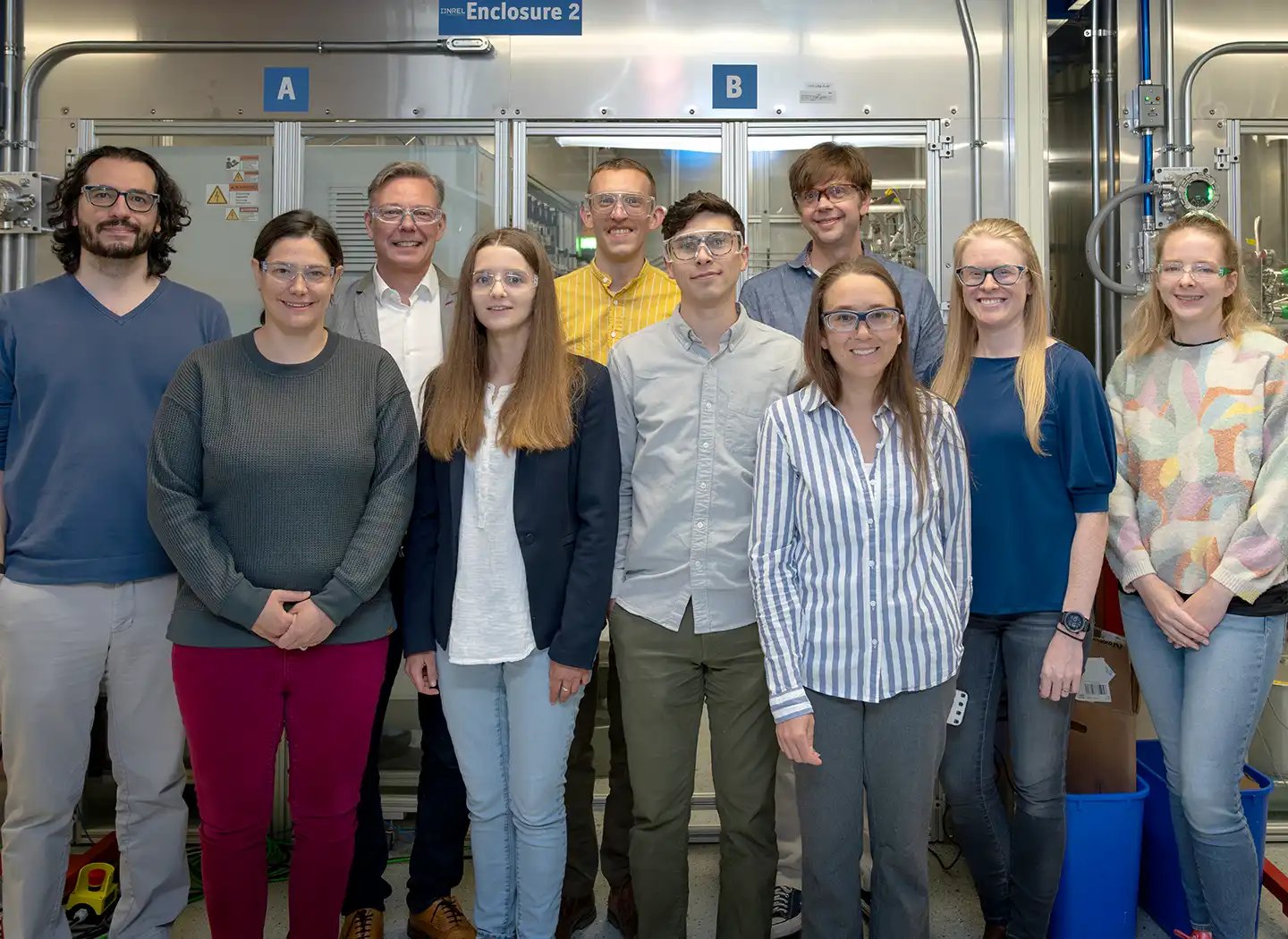 Ten people stand in front of laboratory equipment.