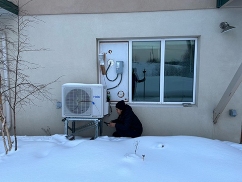 A person works on an air conditioning unit outside in the snow