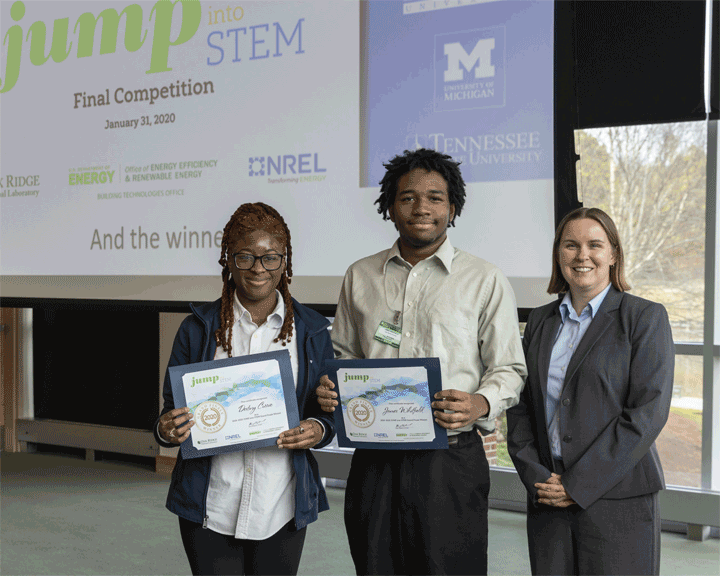 jump-stem-winners-float Photo of two students, holding winner certificates and standing next to an adult in business attire.