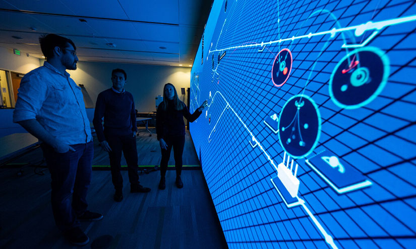 ai-cybersecurity-74764 Three NREL cybersecurity researchers stand in front of a wall-sized projection demonstrating the Advanced Research on Integrated Energy Systems (ARIES).