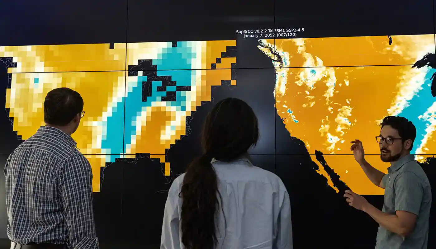 Researchers collaborate in front of a screen of maps.