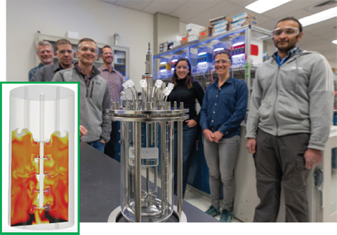 A group of seven individuals stands in a laboratory behind a cylindrical device.