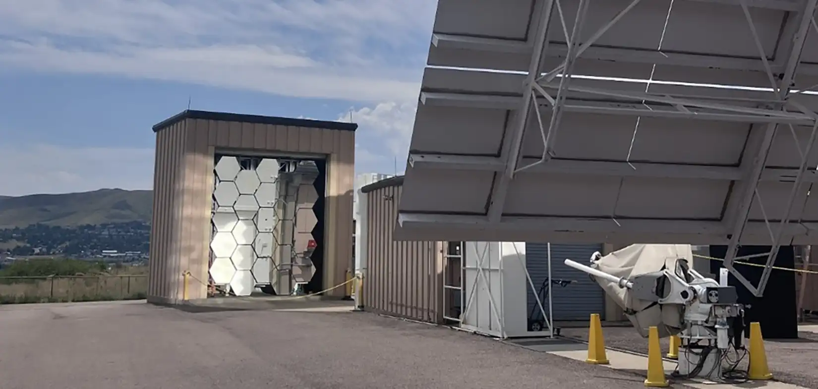 Photo of the high-flux solar furnace concave mirrors and heliostat in front of a blue sky.