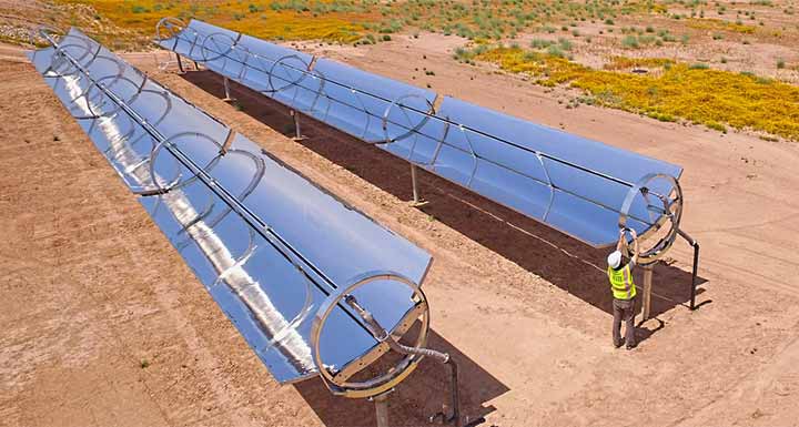 csp-solar-heat-720-thumb A man in a hardhat and reflective vest works on one of two reflective parabolic troughs amidst a desert landscape.