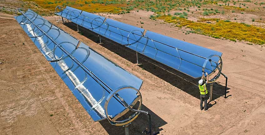 csp-solar-heat-848 A man in a safety gear works on a reflective parabolic trough.