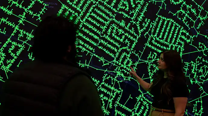 Researcher stands in front of large data display screen and points to grid data