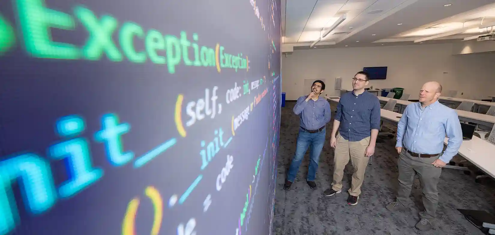 106627-hero Three researchers stand and look up at cybersecurity data displayed on screen