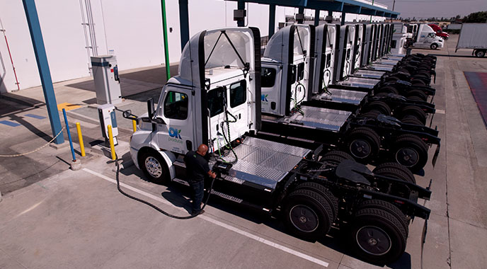 A line of electric eighteen wheeler cabs at charging stations.