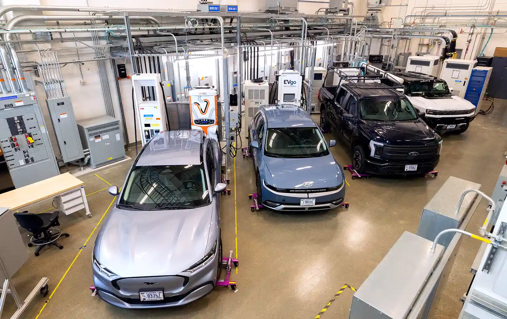 Four cars parked next to chargers inside a laboratory.