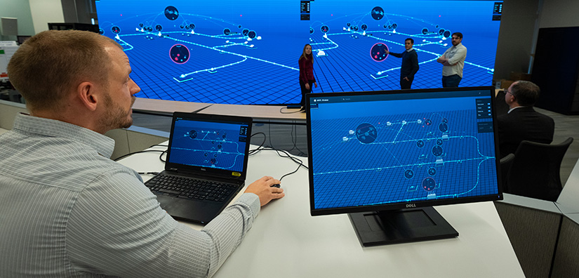 energy-security-74776 Photo of a researcher on the computer sitting at a desk and two researchers standing in front of a large monitor emulating a real-time cyberattack.