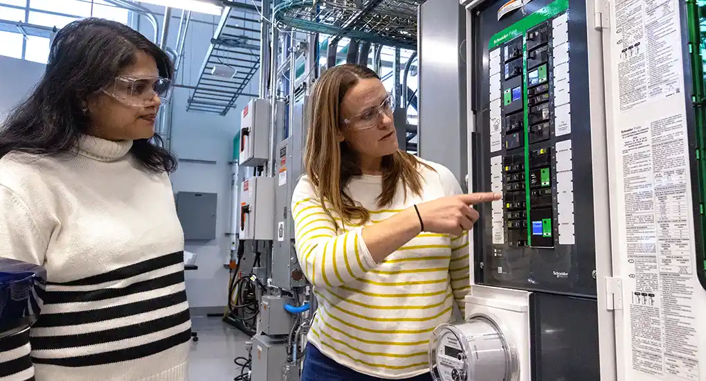 Two women in safety glasses look at control panel inside a laboratory.