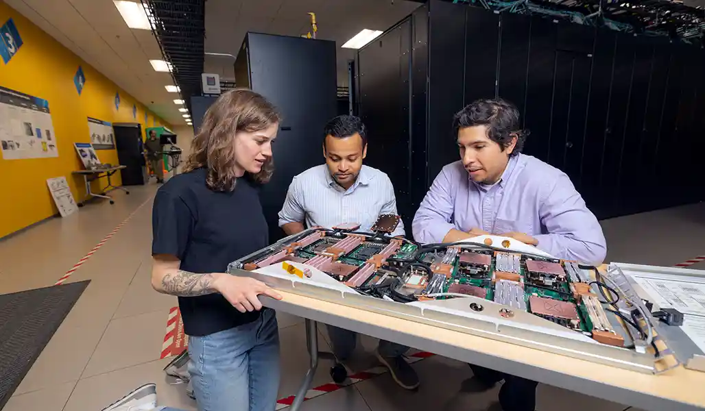 Three researchers look at a blade server supercomputer component inside a lab.