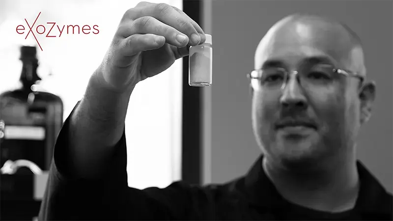 A person in glasses holds up a small vial of white powder.