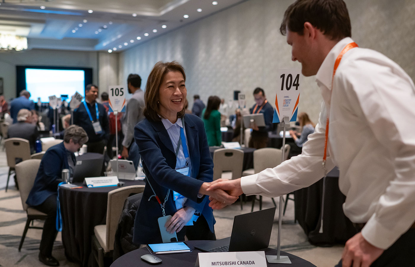 Two people shake hands over a table with a placard reading 'Mitsubishi Canada.'