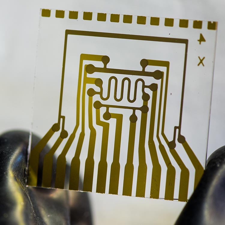 vapor_barrier_diffusion_measurments A photo of a glass square held between two fingers. The glass has a pattern of metal contacts that make up a special electrical circuit. This device represents an electrical calcium test glass card used to measure vapor-barrier permeation rates.