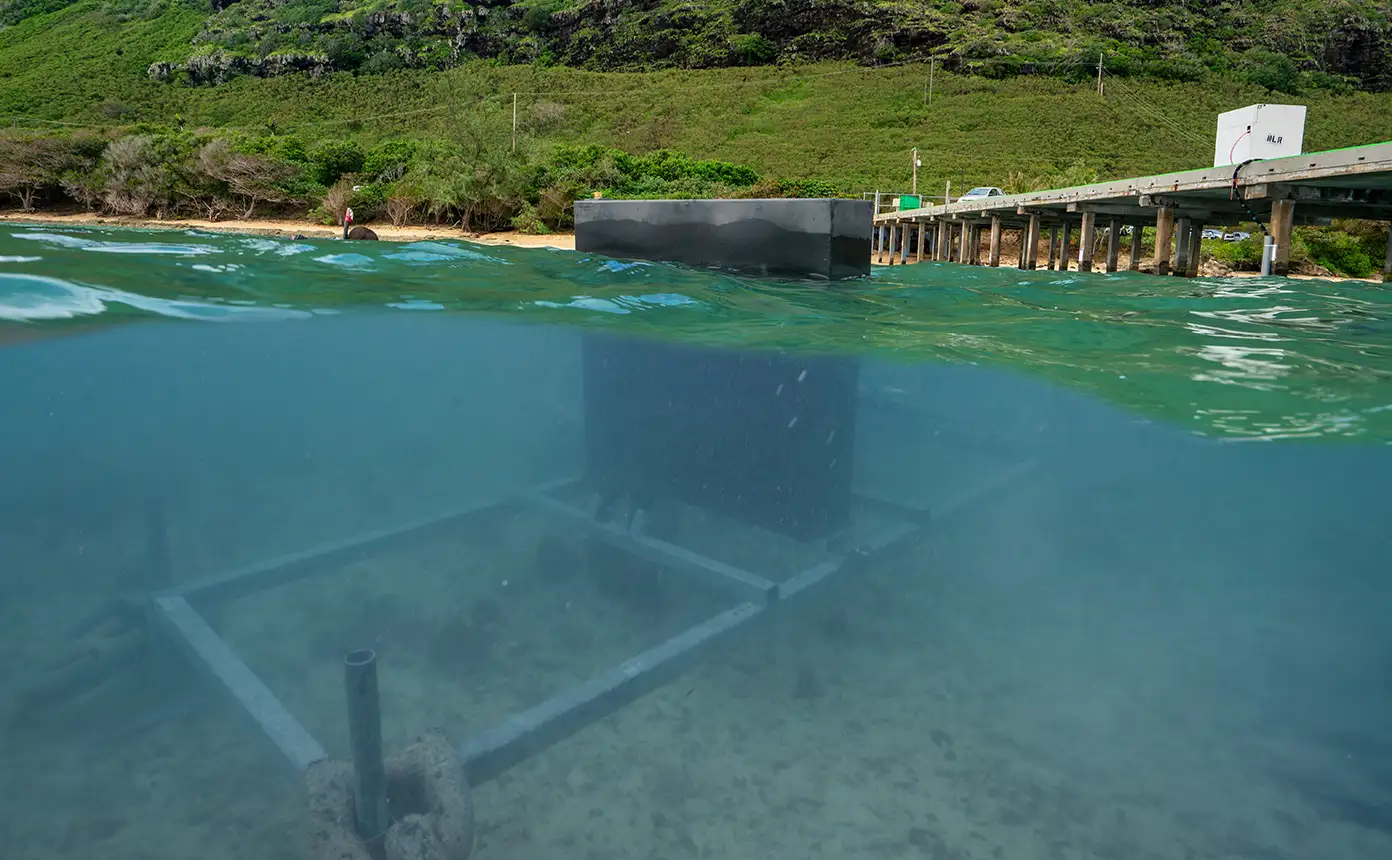 A small underwater research flap wave energy converter device deployed underwater next to a pier off the coast of Hawaii.