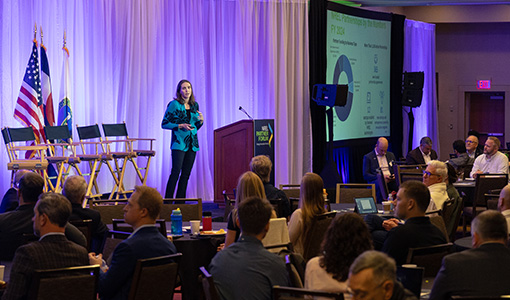 Continue reading about A person stands on a stage in front of a room of people.