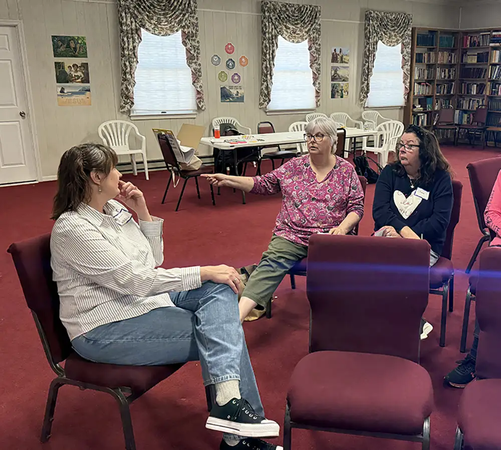 Three people sitting on chairs in a room, talking.