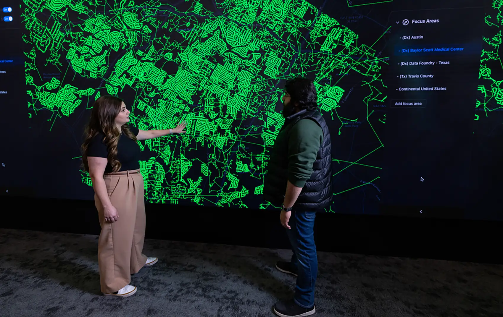 20260310-genesis-missions-ai-driven-research-to-strengthen-us-grid-supply-chains-technological-leadership-97317 Two people stand in front of a map displayed on a full-wall screen.