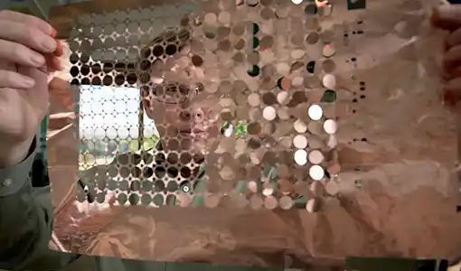 A person holds up a sheet of copper discs.