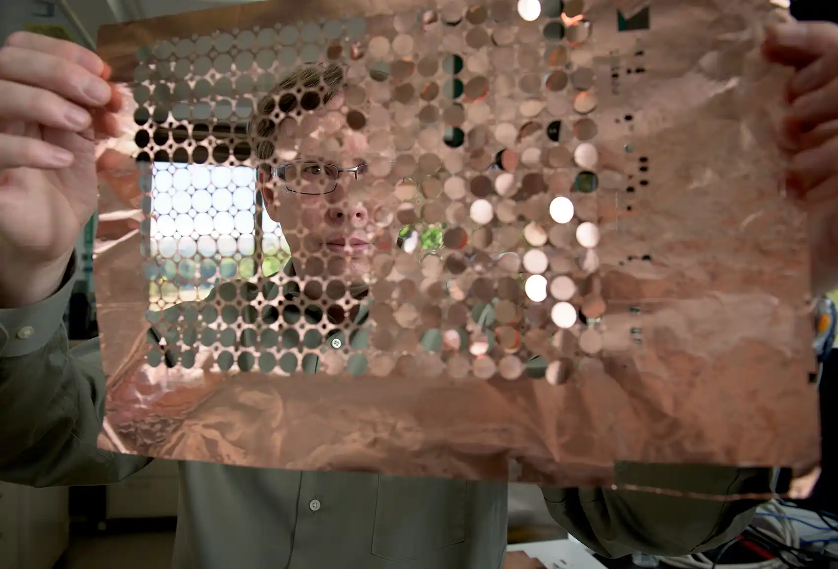 A person holds up a sheet of copper discs.