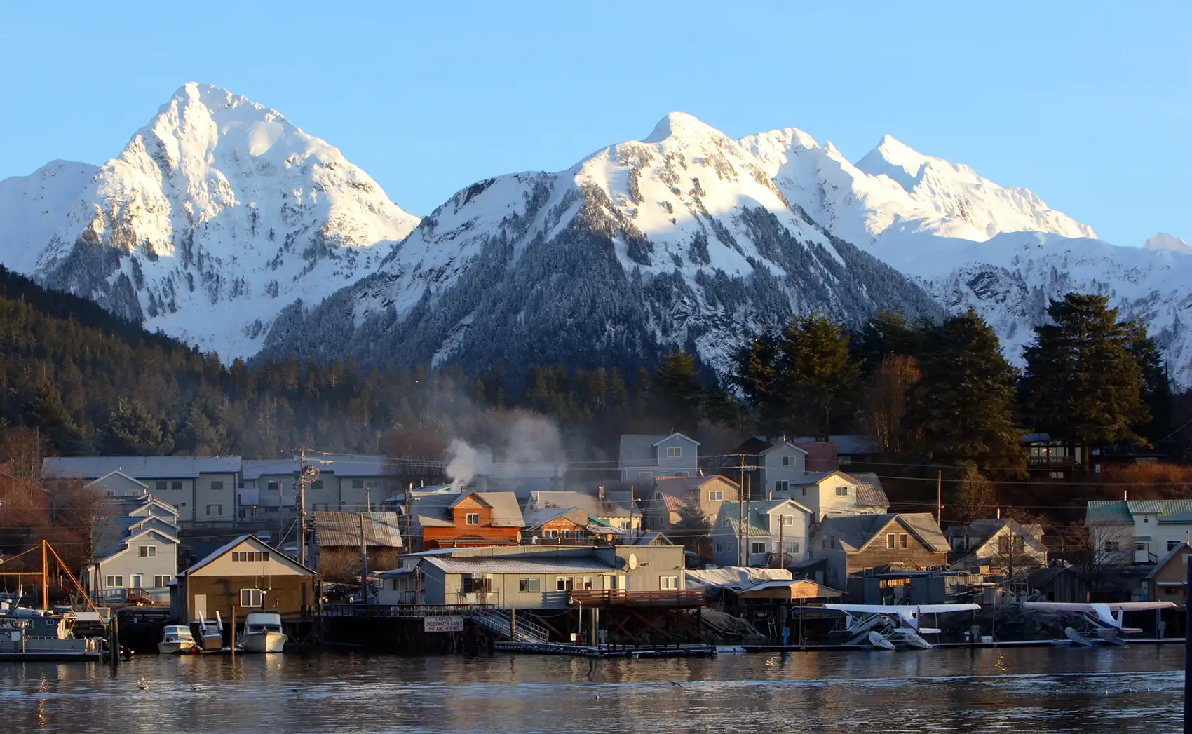 Snowy mountain peaks behind waterfront buildings.