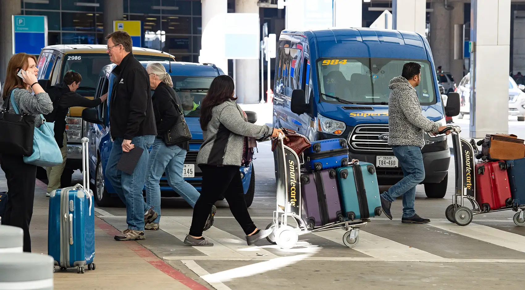 20261021-super-intelligence-speeds-up-transportation-research-at-national-laboratory-of-the-rockies-054640 A busy airport arrivals intersection filled with people crossing a road carrying luggage and locating shuttles.