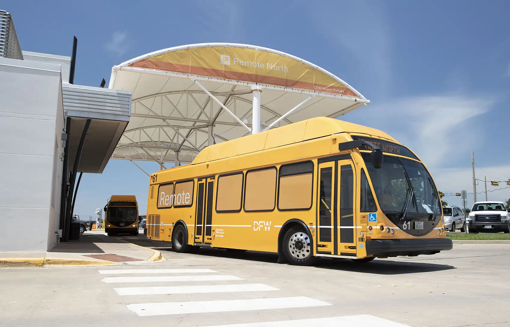 20261021-super-intelligence-speeds-up-transportation-research-at-national-laboratory-of-the-rockies-dfw Two large yellow shuttle buses with Dallas Fort Worth International Airport branding park under an airport awning.