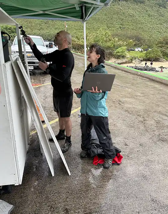 Two researchers examine equipment on a rainy beach.