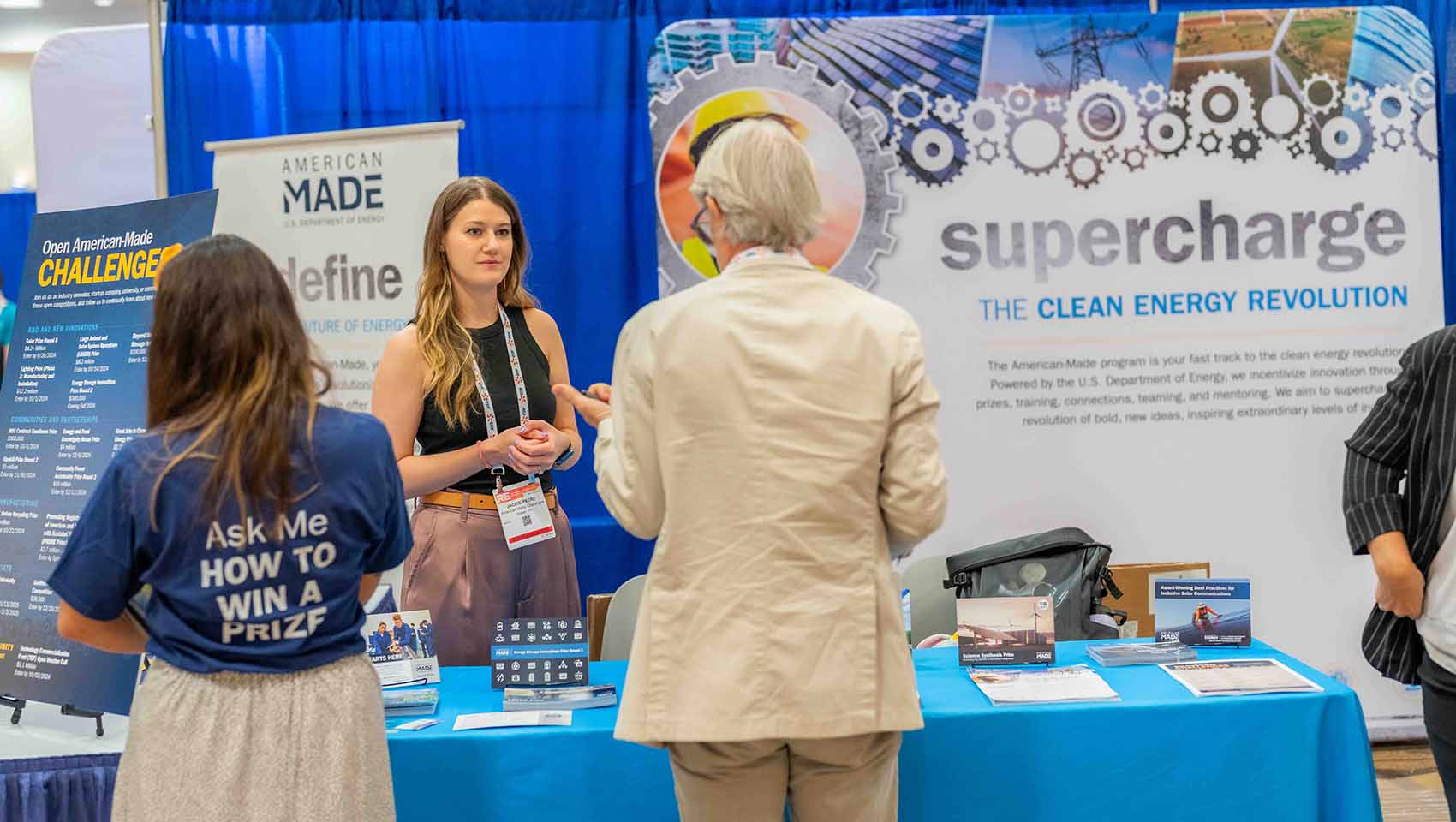 People talking in front of a conference exhibit that says 'supercharge the clean energy revolution'
