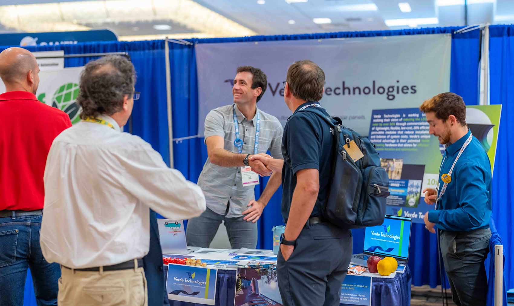 Two people shake hands over a table with three other people standing around them