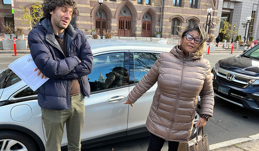 Two people stand in front of an electric vehicle.