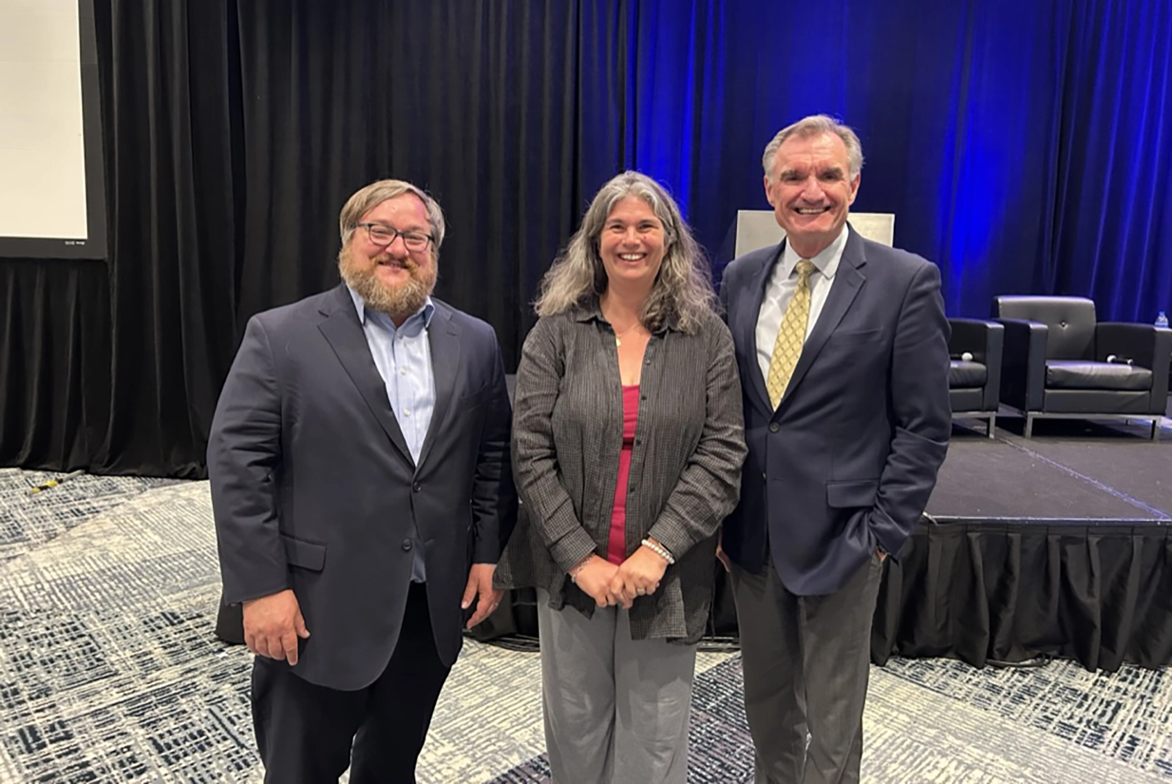 20250722-nrel-transportation-researchers-recognized-for-leadership-innovativeness-collaboration-vehicle-technologies-office-annual-merit-reviews Three people pose in front of a stage.
