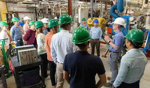 Continue reading about A group of people wearing hard hats stand in a lab.