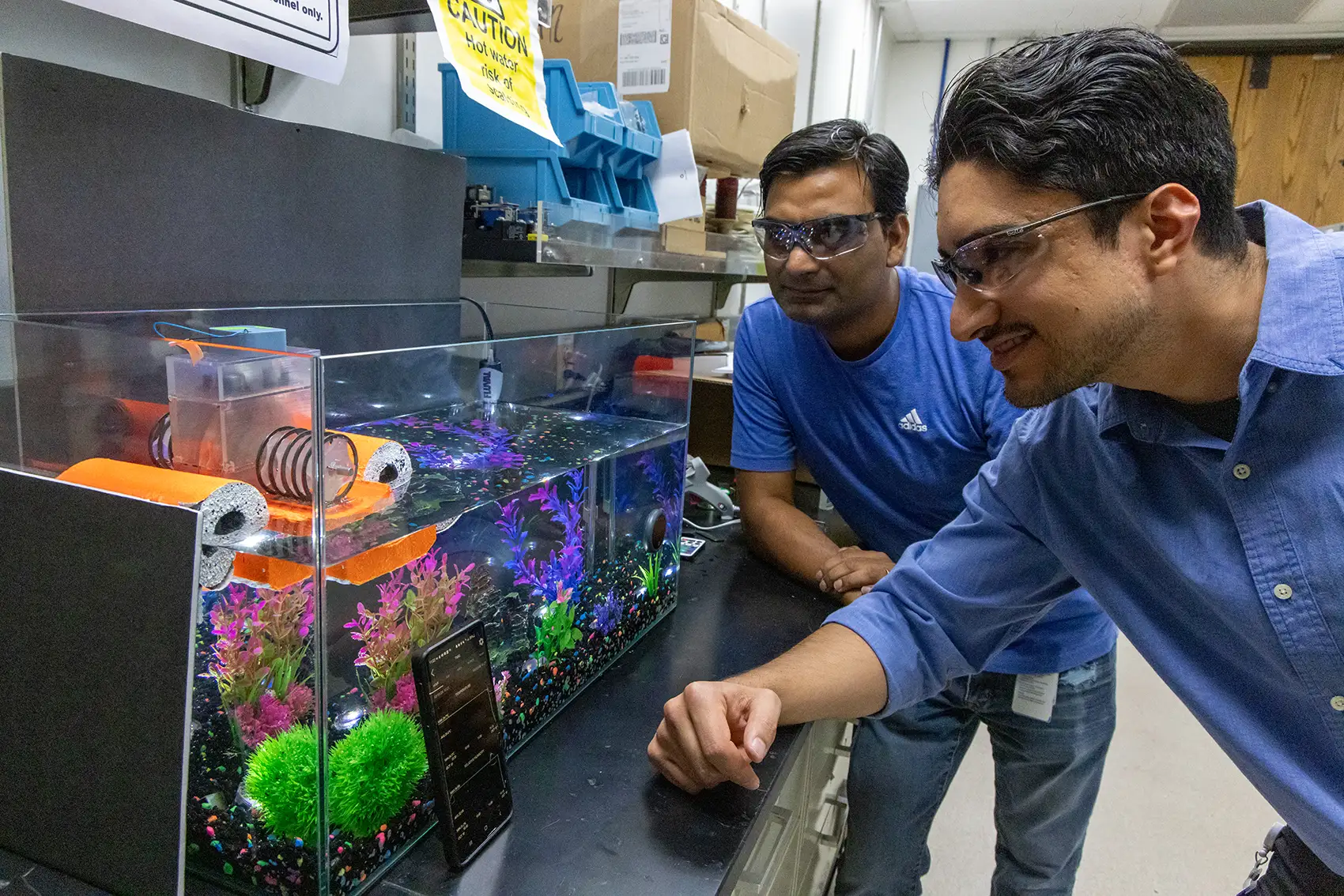 Two men examine a device floating on top of a fish tank.