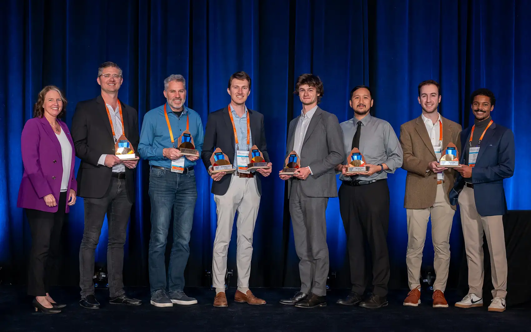Eight people stand on a stage holding trophies.