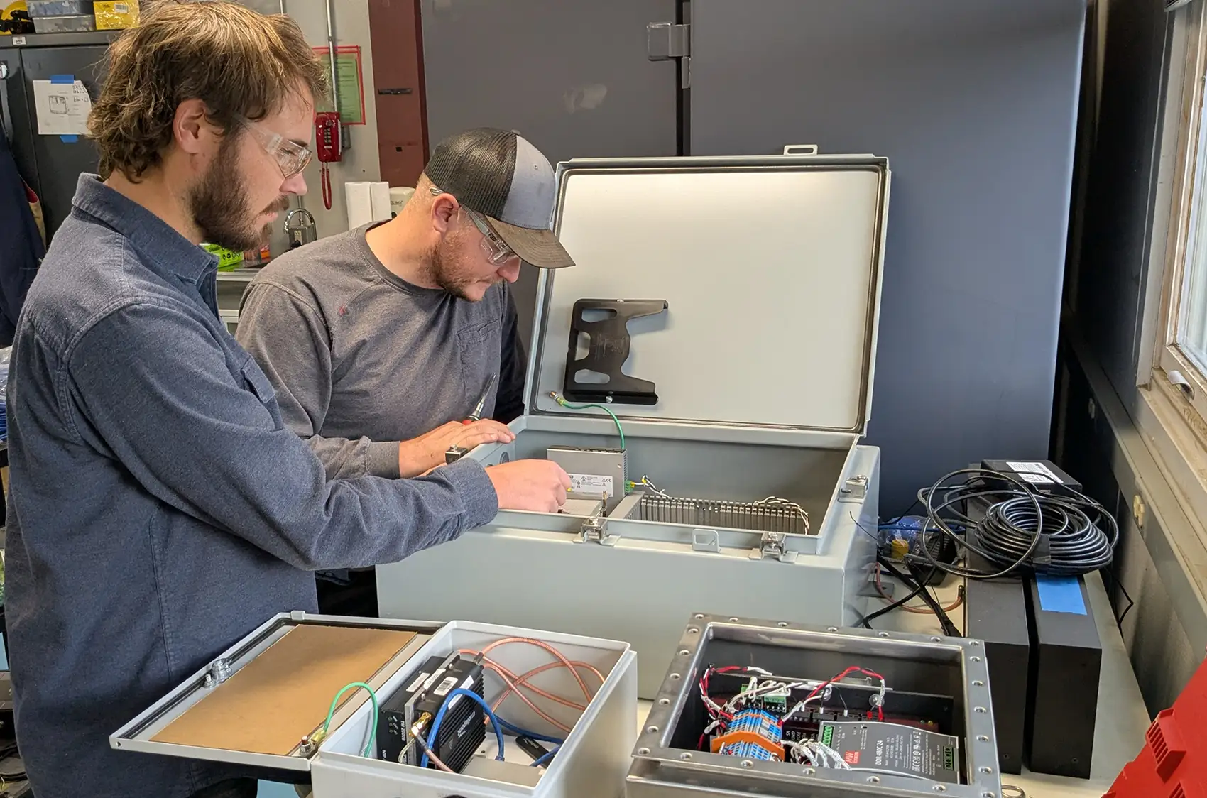 20260209-how-to-crack-the-wave-energy-code-swartz-nichols Two people look inside a box containing machinery.