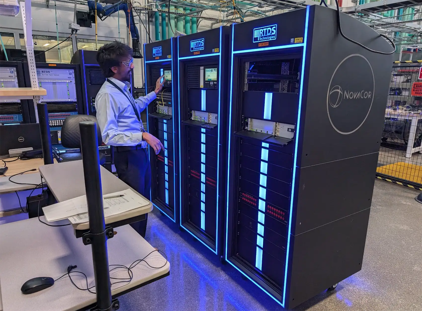 A person wearing safety goggles standing next to three server racks