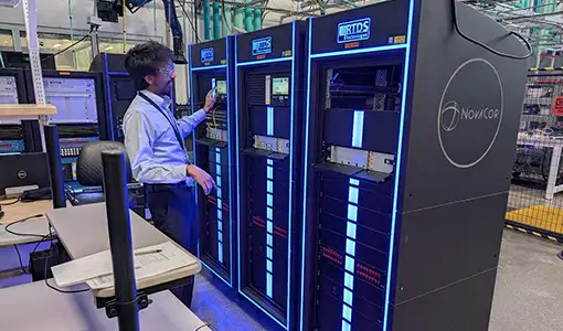 Continue reading about A person wearing safety goggles standing next to three server racks