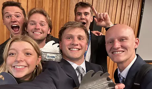 Continue reading about A team of six smiling student competitors pose for a selfie. Three students are holding metal trophies featuring a wave design