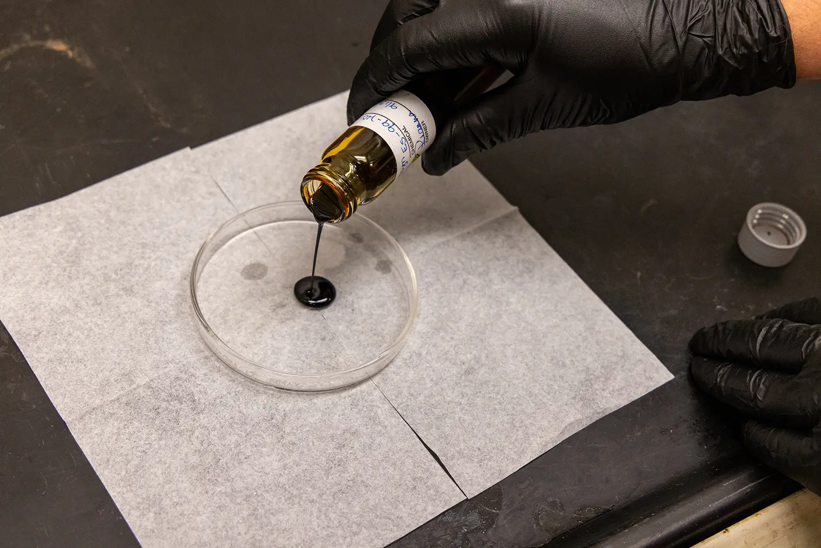 20260325-turning-biomass-into-graphite-could-help-secure-us-critical-mineral-supply-pyrolysis-oil-094297 A researcher pours black pyrolysis oil into a petri dish.