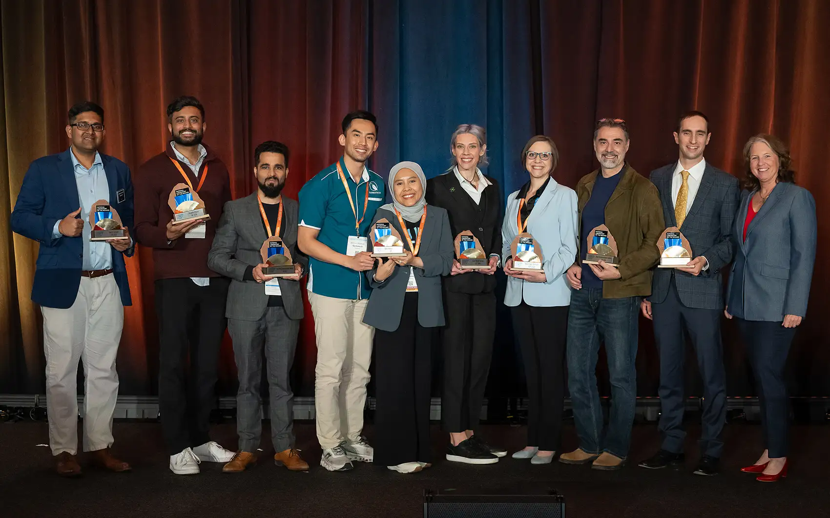 Ten people holding trophies standing on a stage.