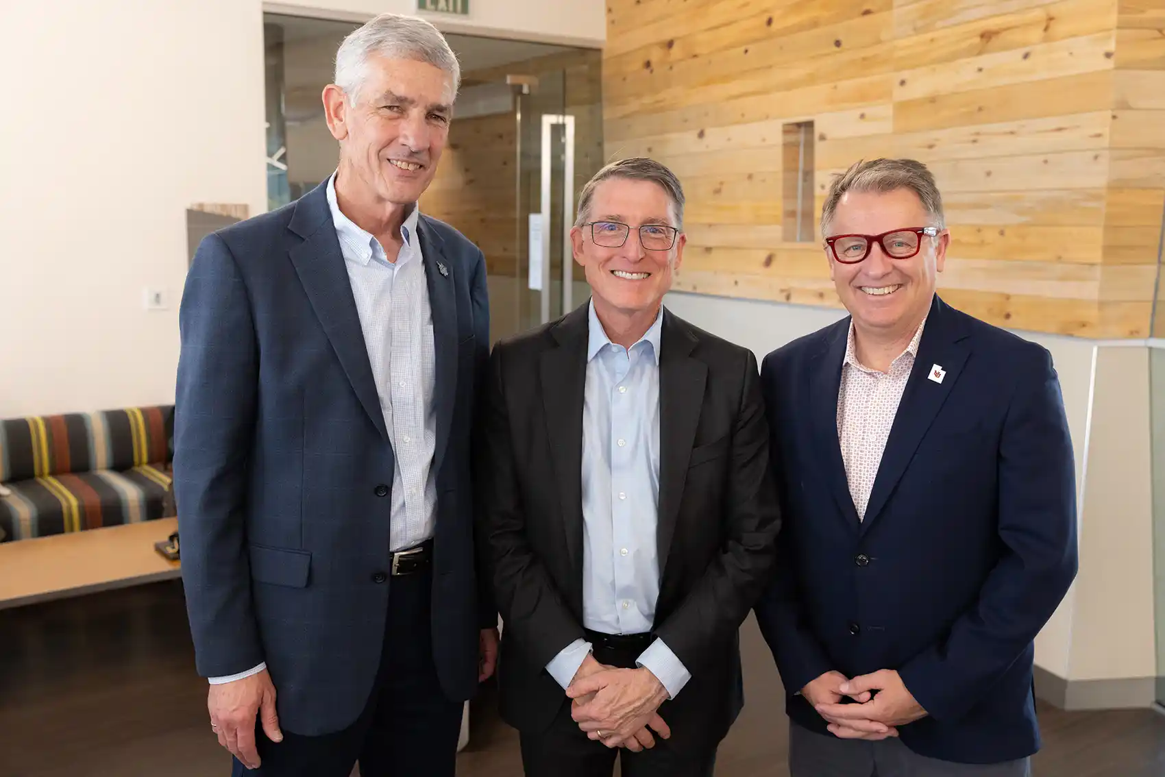 Three people wearing suits smiling.
