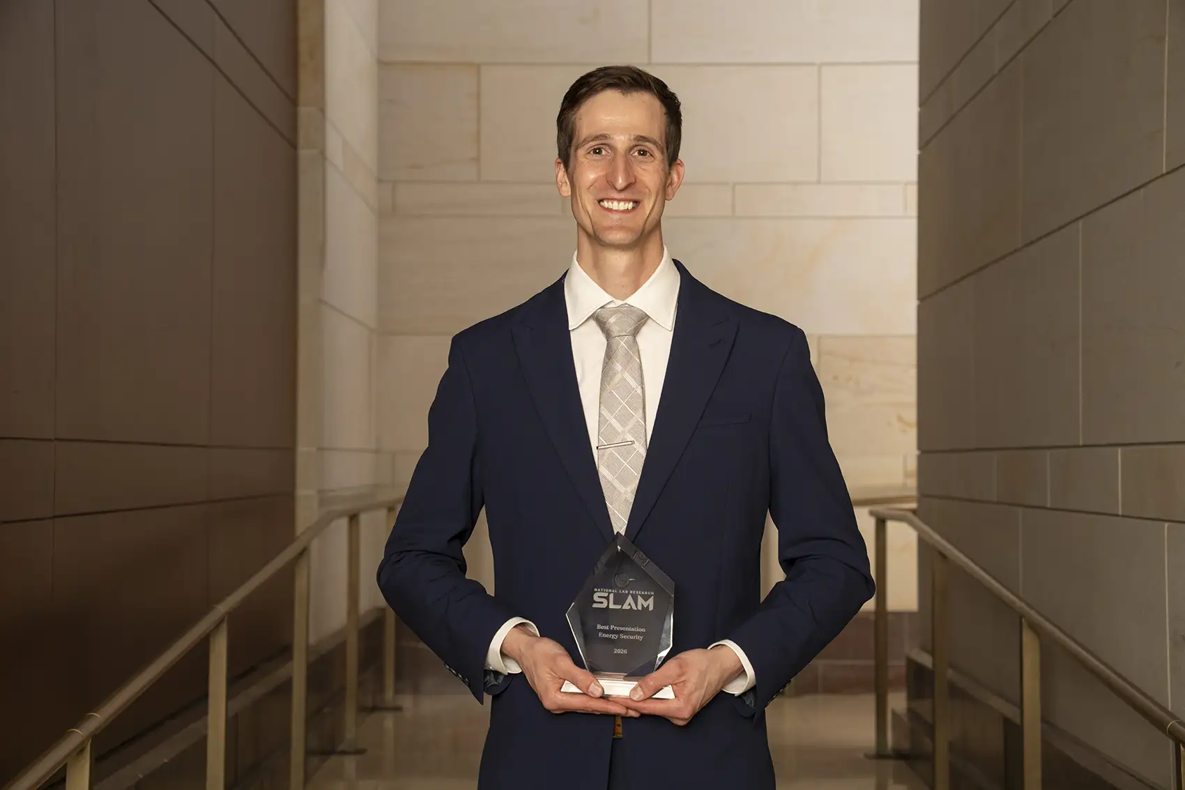 A person in a suit and tie holding an award and smiling at the camera