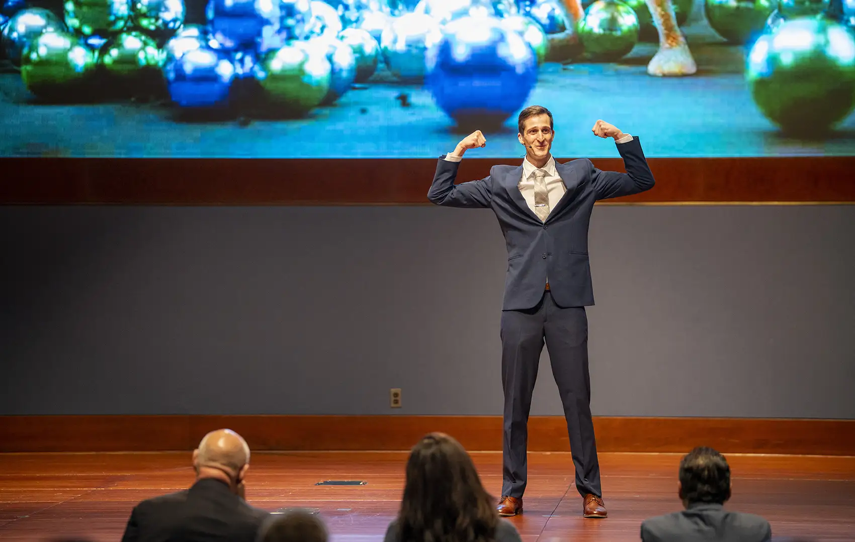 A person in a suit flexes his arms on stage