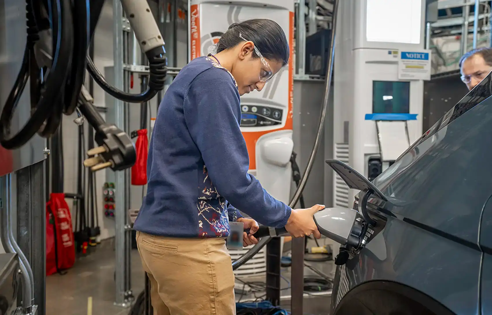 A person plugs a charging cable into a vehicle in a lab.