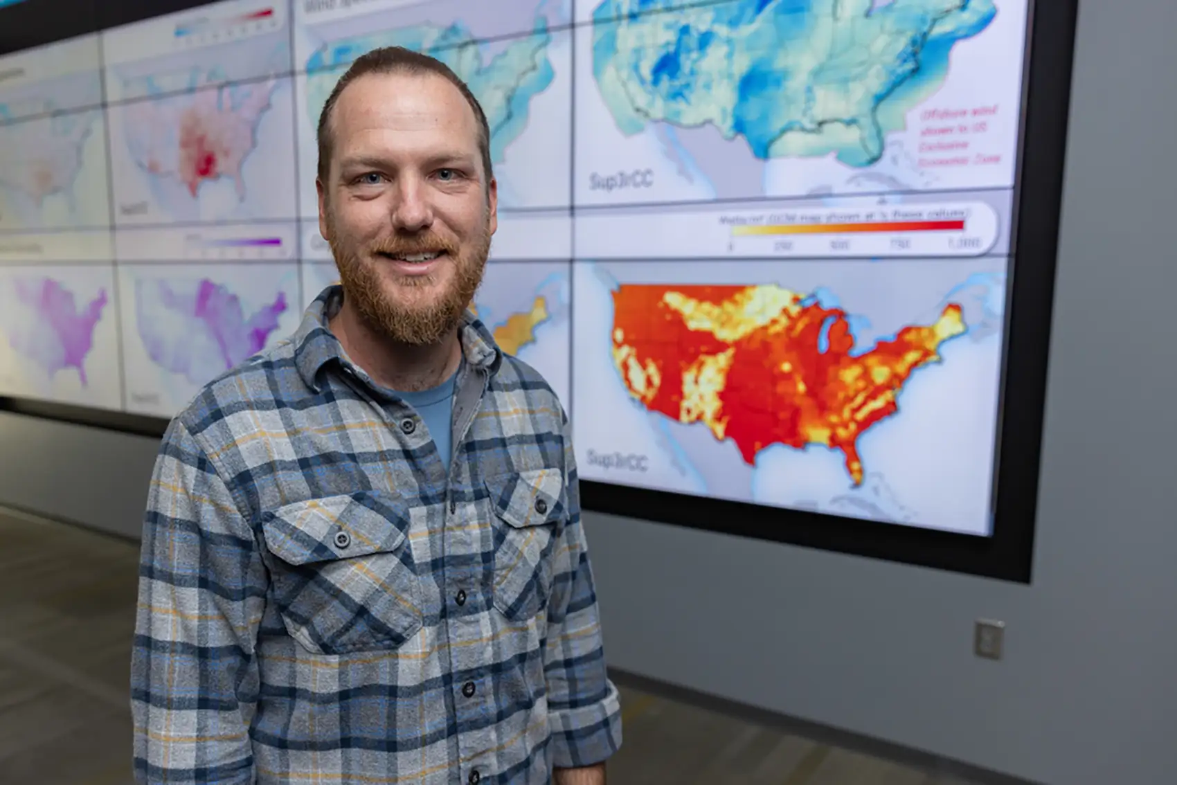 20260601-ai-research-digs-deep-into-mining-operations-83590 Ryan King in front of a wall of screens with maps of the United States on them.