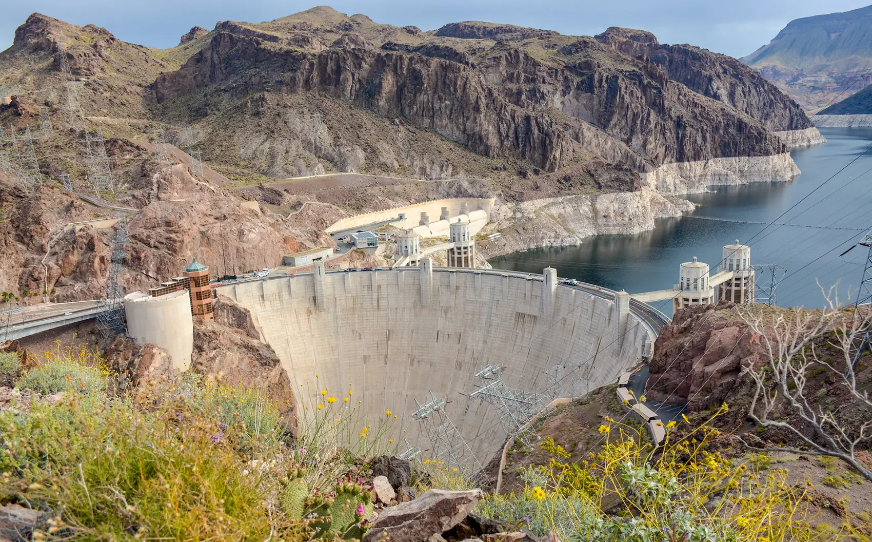 A photo with mountains, water, a dam, and plants.